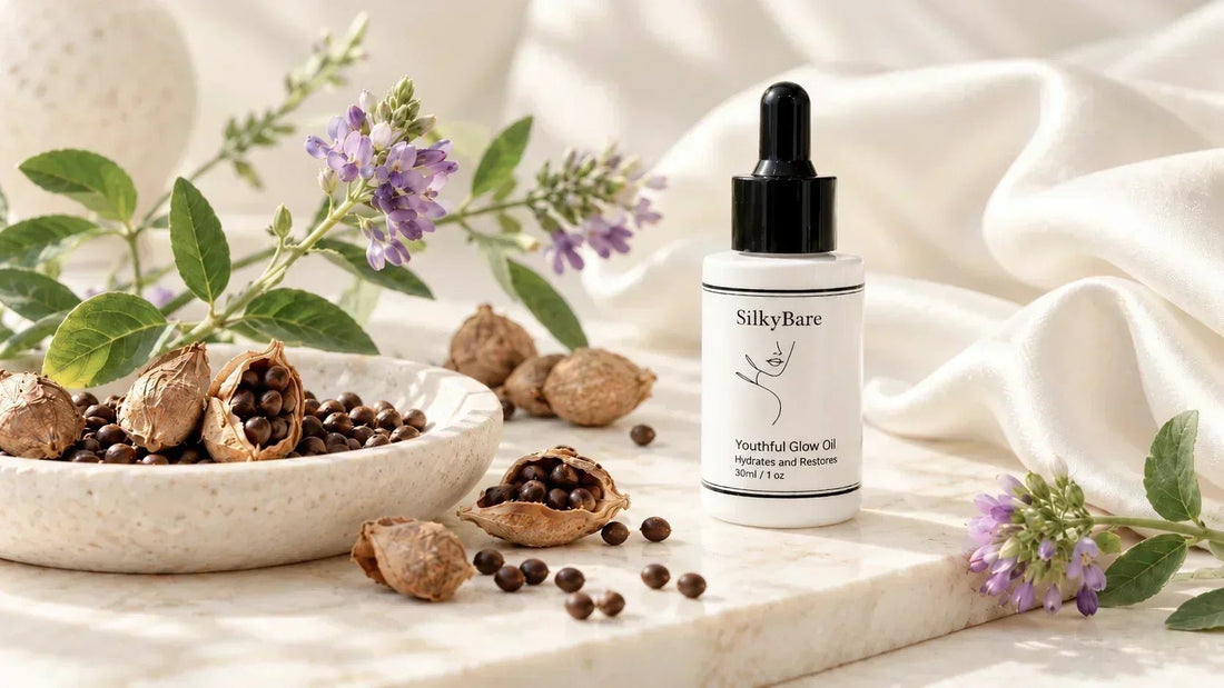 SilkyBare face oil with bakuchiol beside purple flowers, seed pods and seeds on a cream surface.