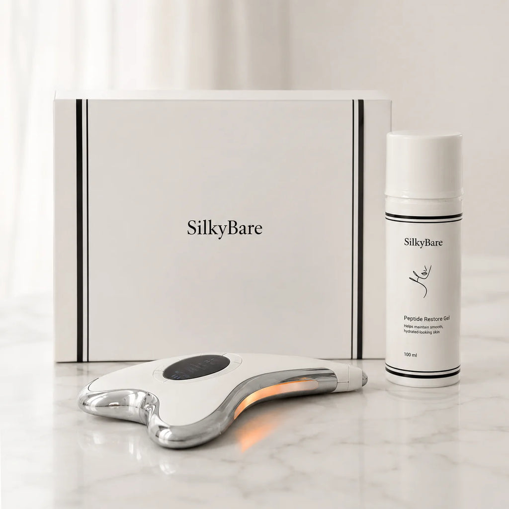 SilkyBare skincare set on a light marble surface, featuring a white and silver facial massage device, a white peptide gel bottle, and a white branded box in the background.