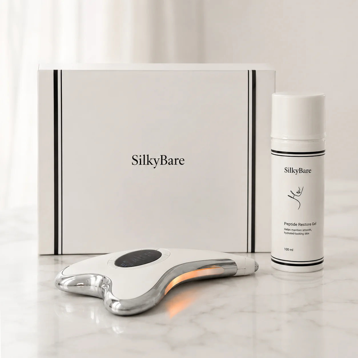 SilkyBare skincare set on a light marble surface, featuring a white and silver facial massage device, a white peptide gel bottle, and a white branded box in the background.