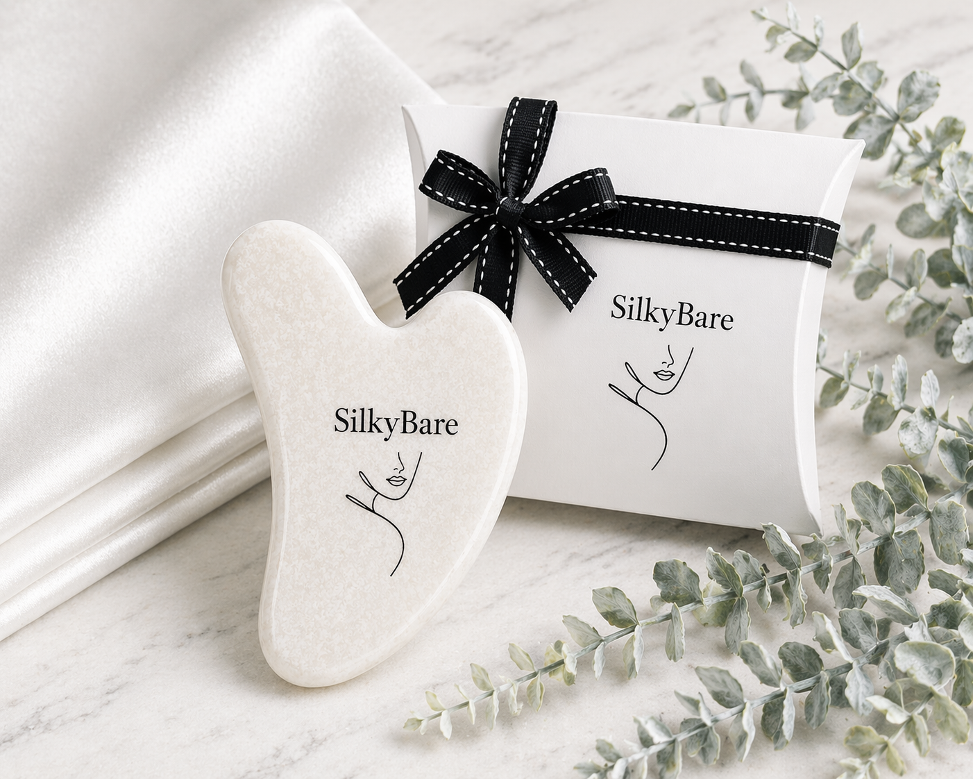 SilkyBare gua sha tool with packaging on white silk pillowcase and gift box