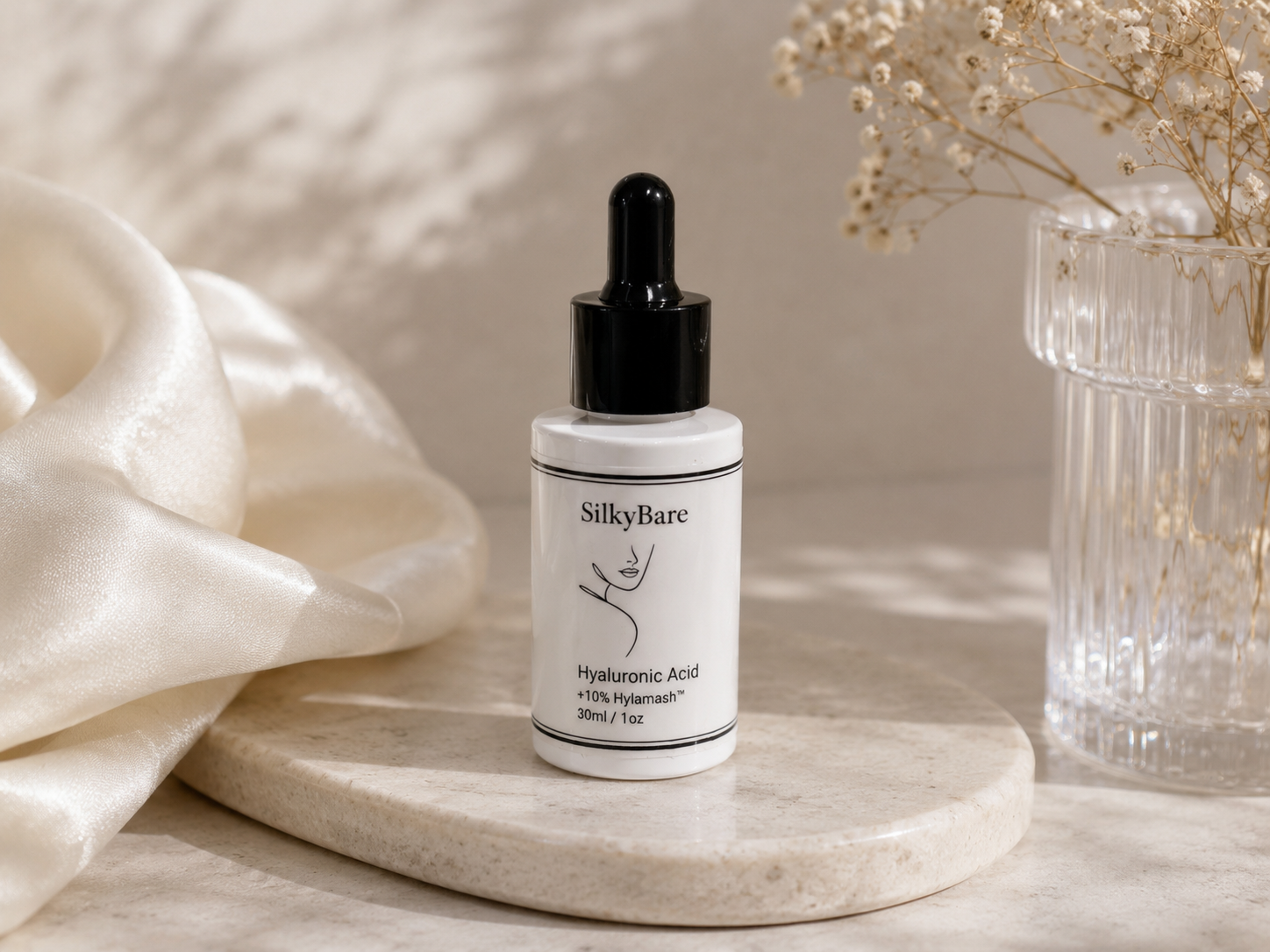 SilkyBare hyaluronic serum sits on a marble tray, glass vase and silk background